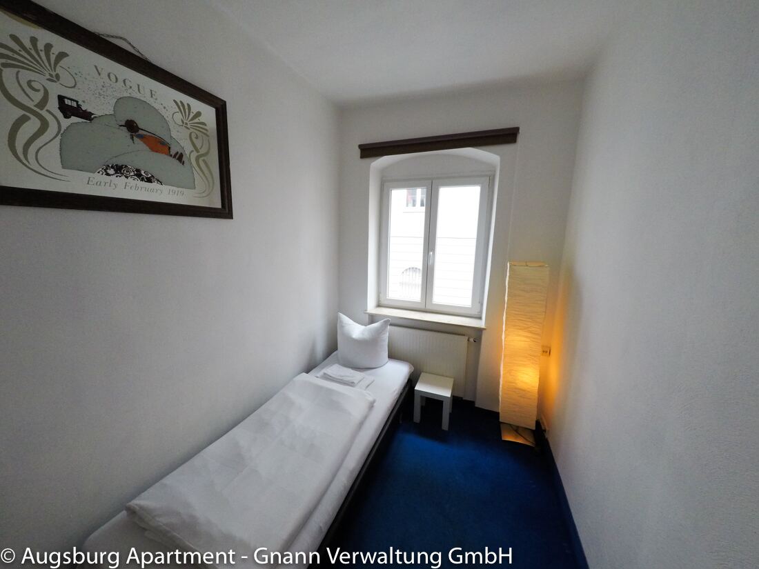 Kleines Einzelzimmer mit Bett und Stehlampe in einem möblierten Apartment in Augsburg